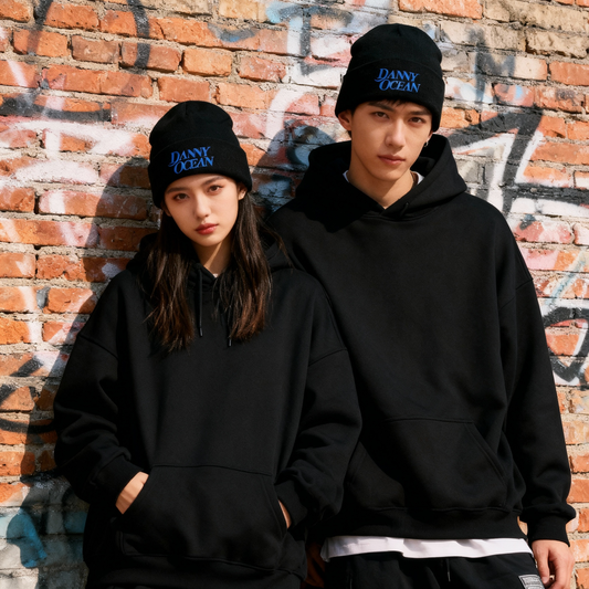 Fotografía de estilo de vida con pareja luciendo el beanie de Danny Ocean frente a una pared de ladrillo, resaltando el logo bordado del artista