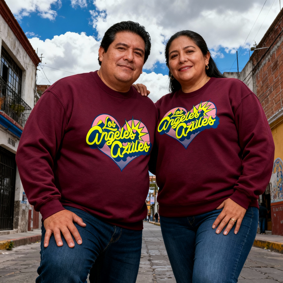 Pareja luciendo la mercancía oficial de Los Ángeles Azules para su gira por Estados Unidos, mostrando el diseño de corazón en el pecho.