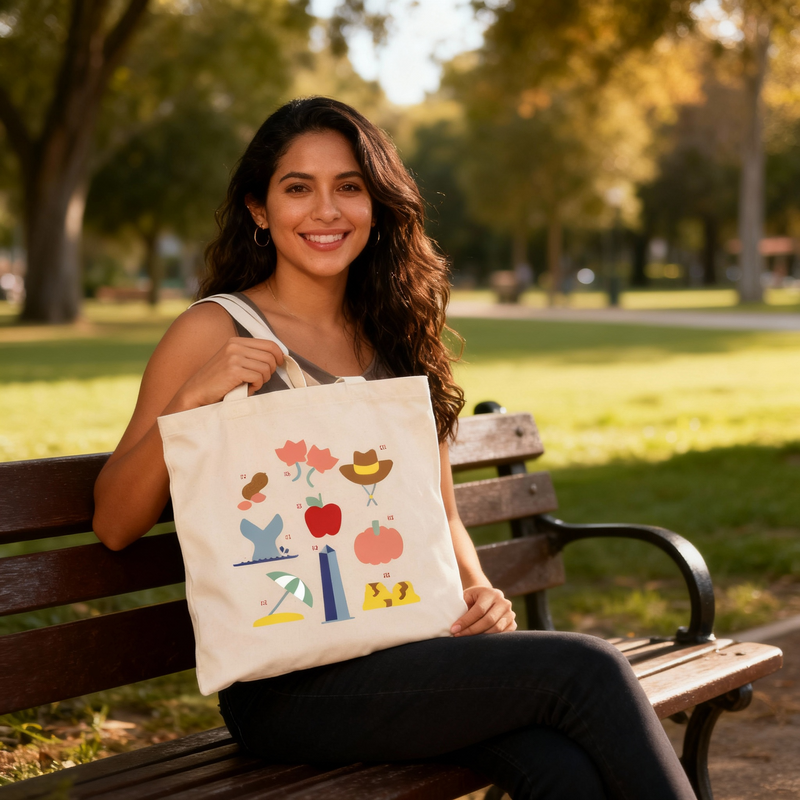 Fotografía en plano medio (medium shot) de una modelo mujer sentada de frente en una banca de madera en un parque, sosteniendo la tote bag ilustrada de Ximena Sariñana.