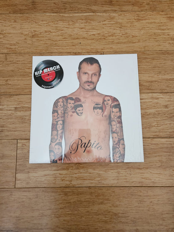 Fotografía de la portada frontal del vinilo Papito de Miguel Bosé sobre un piso de madera, mostrando el arte del álbum y un sticker circular negro en la esquina superior izquierda.