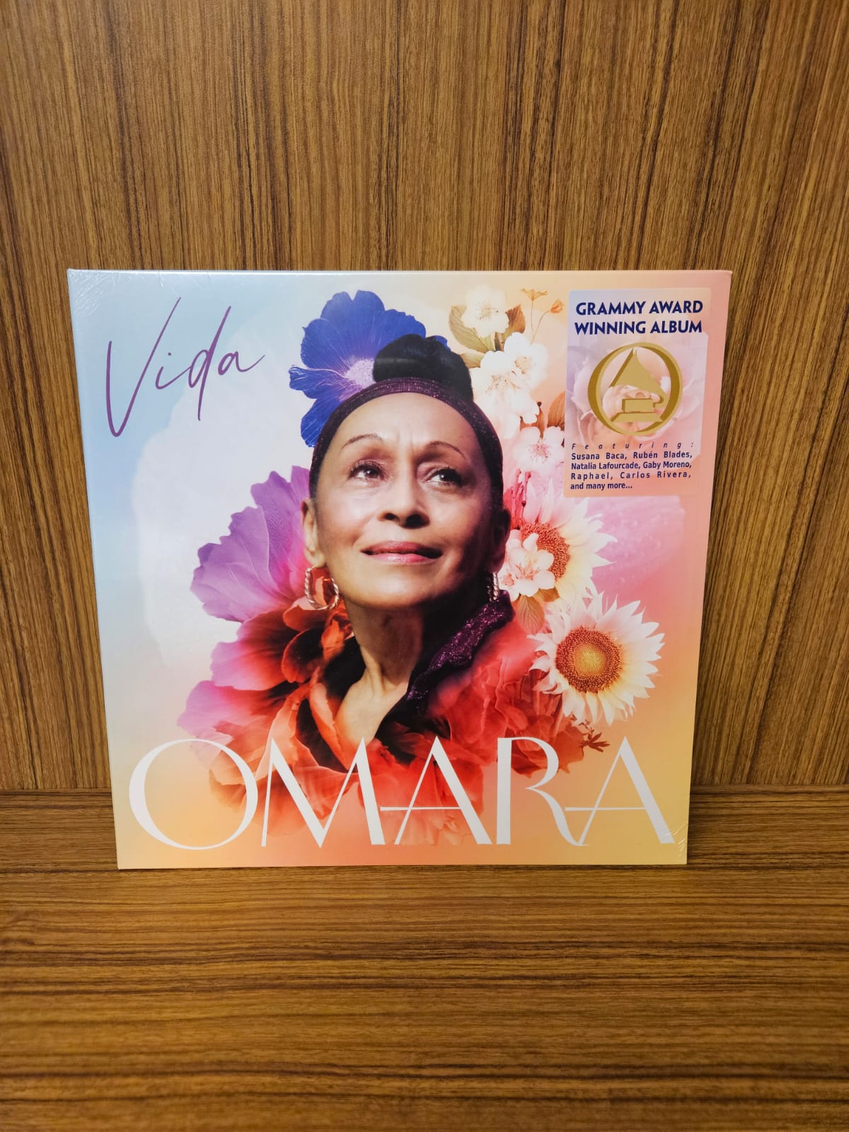 Fotografía de la portada frontal del vinilo VIDA de Omara Portuondo, mostrando el arte gráfico a color y el sticker dorado de fondo sobre una superficie de madera.