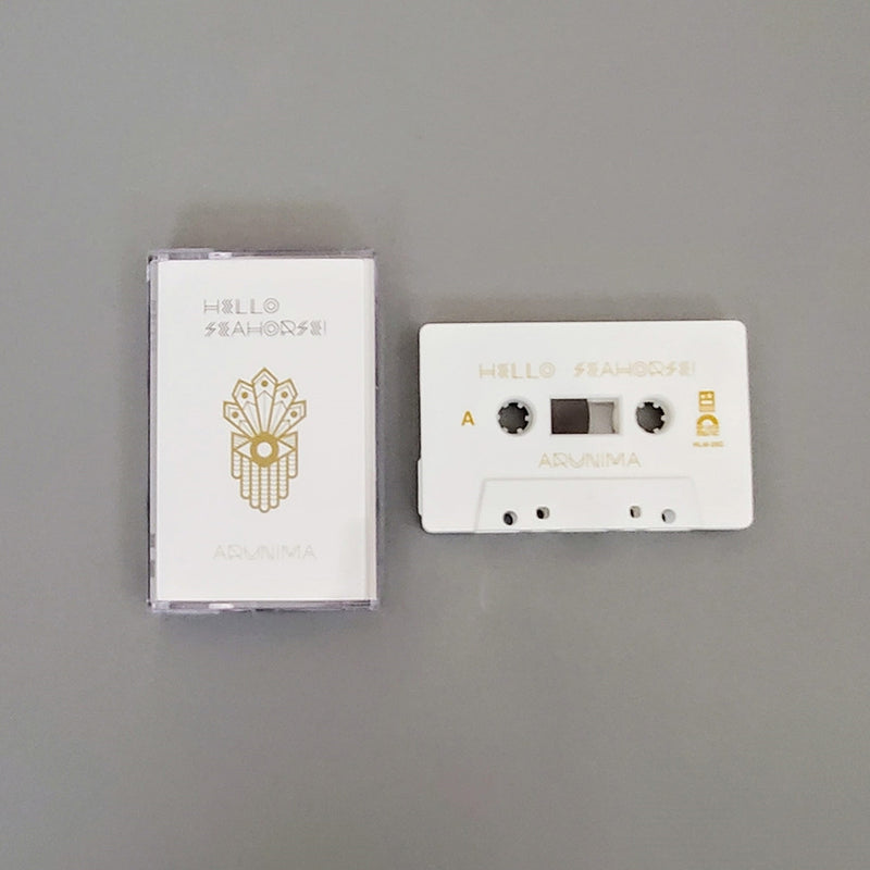 Fotografía de la edición limitada en cassette del álbum Arunima de Hello Seahorse!, exhibiendo la cinta física en color blanco con detalles dorados junto a su estuche oficial.