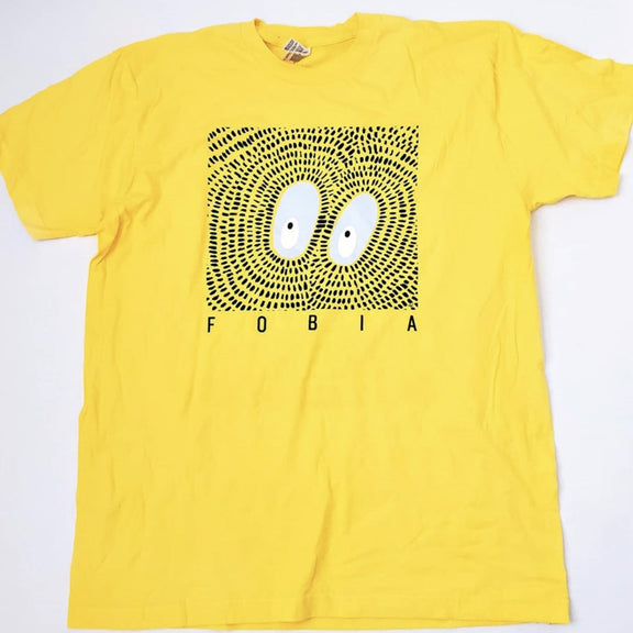 Fotografía de la vista frontal de la playera amarilla oficial de Fobia, mostrando el diseño textil de cuello redondo con un estampado gráfico alusivo a la banda en el pecho.