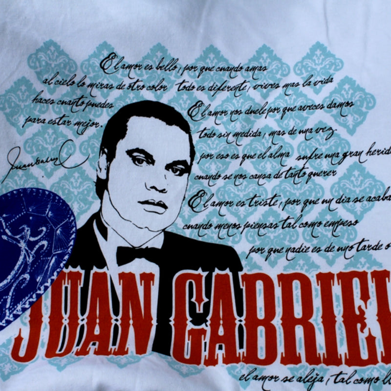 Acercamiento detallado al estampado de la playera que muestra el retrato de Juan Gabriel, un sombrero charro azul, letras rojas y texturas de fondo.