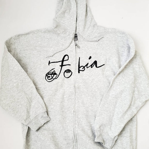 Fotografía de la vista frontal de la sudadera gris claro oficial de Fobia, mostrando el diseño con cierre, capucha y el logotipo de la banda estampado en color negro.