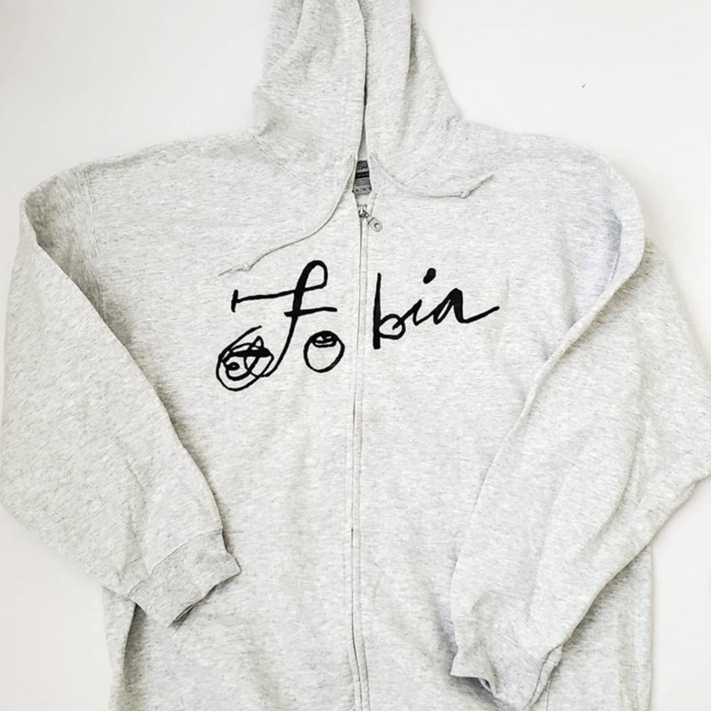 Fotografía de la vista frontal de la sudadera gris claro oficial de Fobia, mostrando el diseño con cierre, capucha y el logotipo de la banda estampado en color negro.